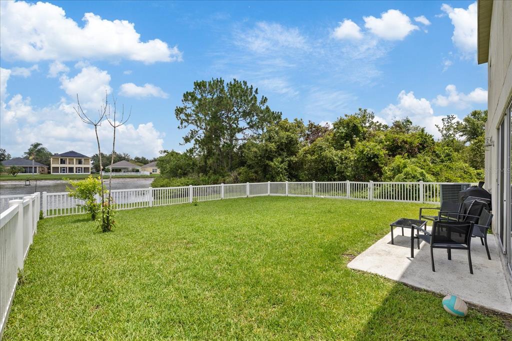 A grassy backyard features a white picket fence, a concrete patio, and a water view — 9467 LEATHERWOOD AVENUE, TAMPA, FL