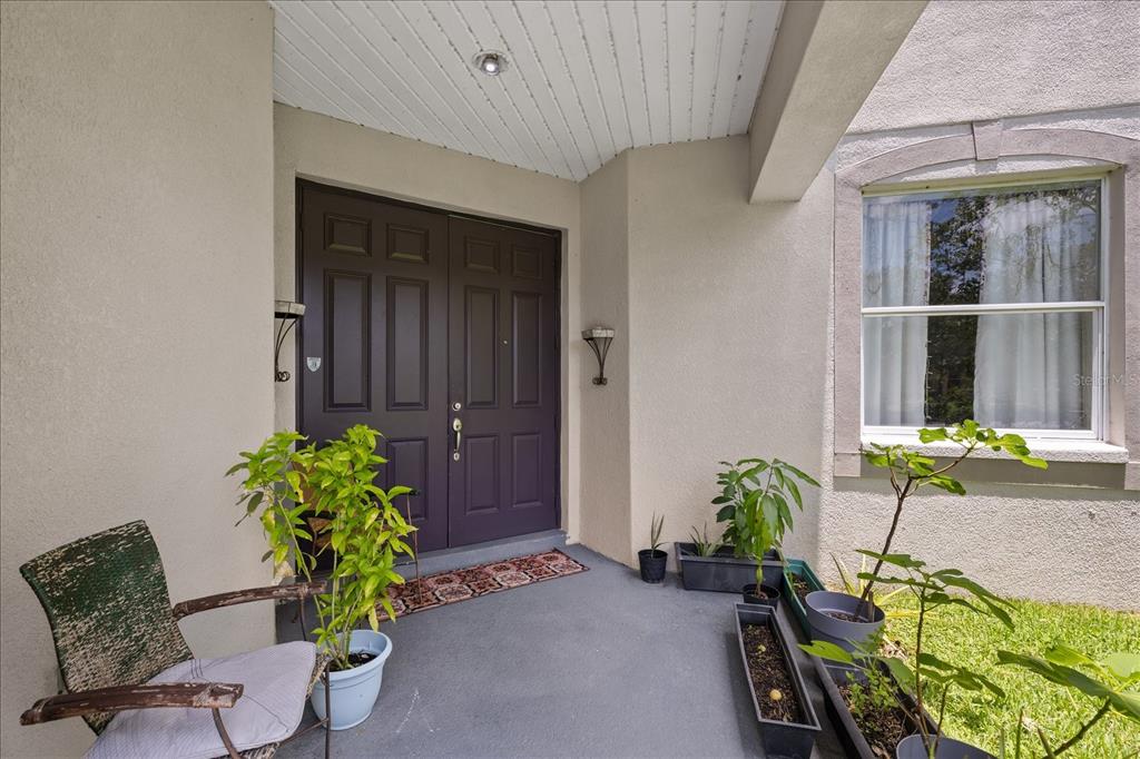 A covered front porch features a double door entrance, a chair, and several potted plants — 9467 LEATHERWOOD AVENUE, TAMPA, FL