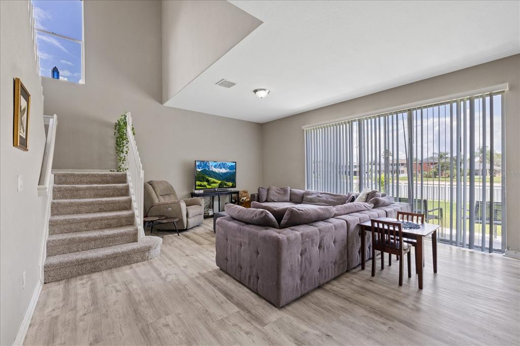 A living room with light wood flooring, a sectional sofa, stairs, and large sliding glass doors — 9467 LEATHERWOOD AVENUE, TAMPA, FL