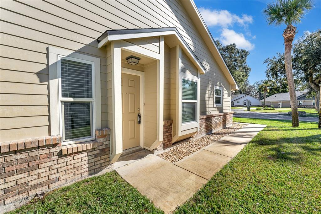 The exterior of a tan house features a covered entryway, brick accents, and a concrete walkway — 233 BOB WHITE COURT, DAYTONA BEACH, FL