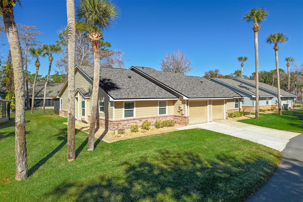 A tan, single-story house with a brick base, two garage doors, and several palm trees — 233 BOB WHITE COURT, DAYTONA BEACH, FL