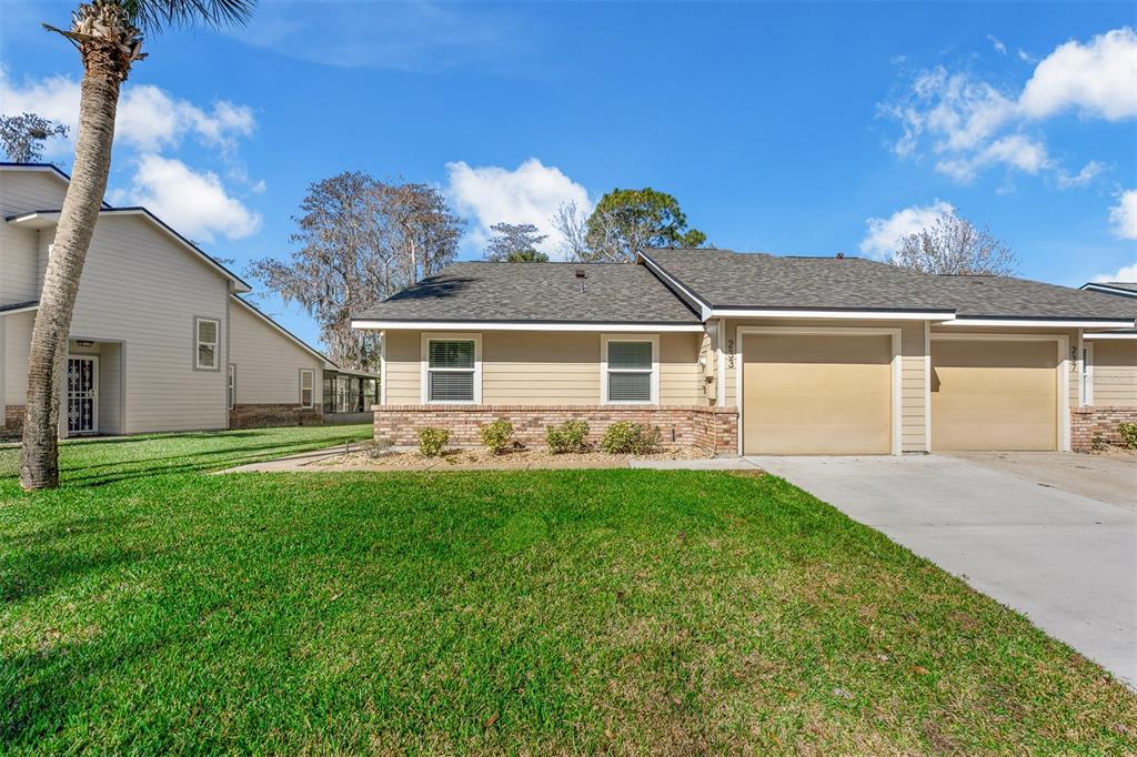 A tan single-story duplex with a brick base, two garage doors, and a grassy lawn — 233 BOB WHITE COURT, DAYTONA BEACH, FL