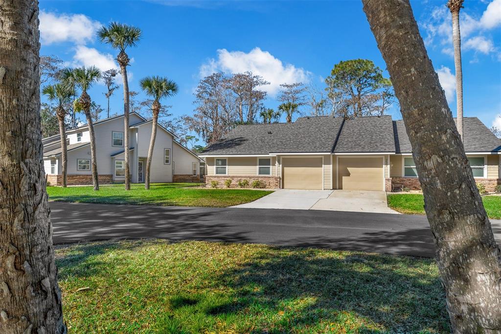 A view of two residential buildings with tan siding, garages, and palm trees on a lawn — 233 BOB WHITE COURT, DAYTONA BEACH, FL