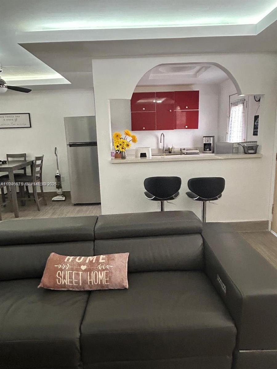 A living room features a dark sofa facing a kitchen with red cabinets and bar seating — 16900 NE 14th Ave # 209, Miami FL 33162, MIAMI, FL