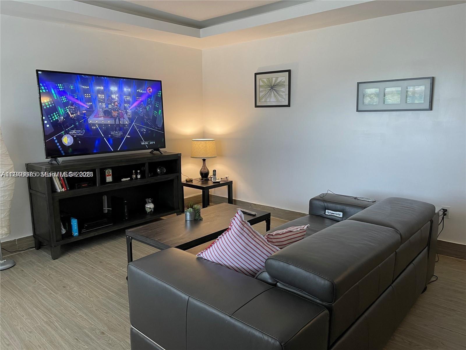 A living room features a dark leather sofa, a television on a stand, and wood-look flooring — 16900 NE 14th Ave # 209, Miami FL 33162, MIAMI, FL