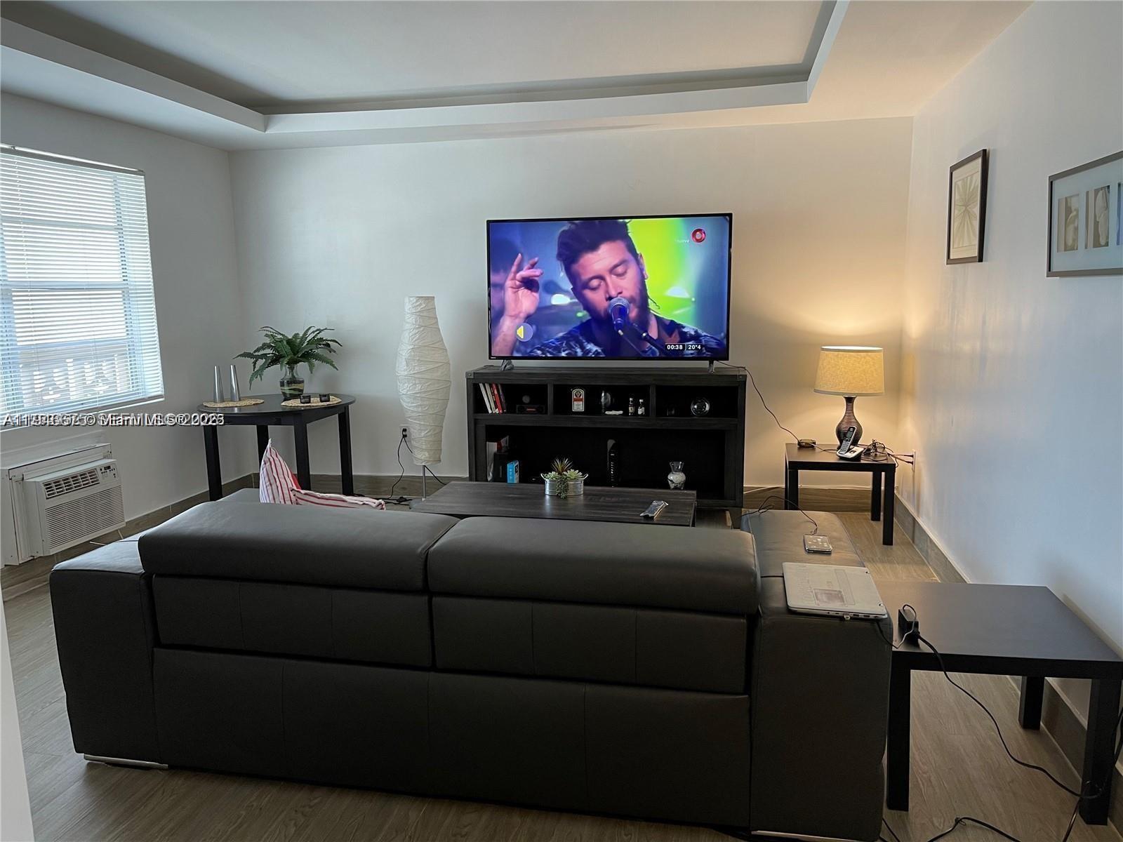 A living room features a dark leather sofa, a television on a stand, and wood-look flooring — 16900 NE 14th Ave # 209, Miami FL 33162, MIAMI, FL