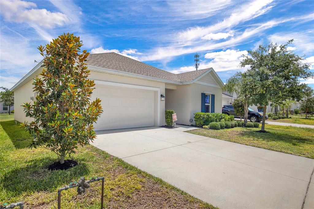 A single-story house with a two-car garage, beige stucco exterior, and a concrete driveway — 3078 BLUE BONNET LANE, OSTEEN, FL