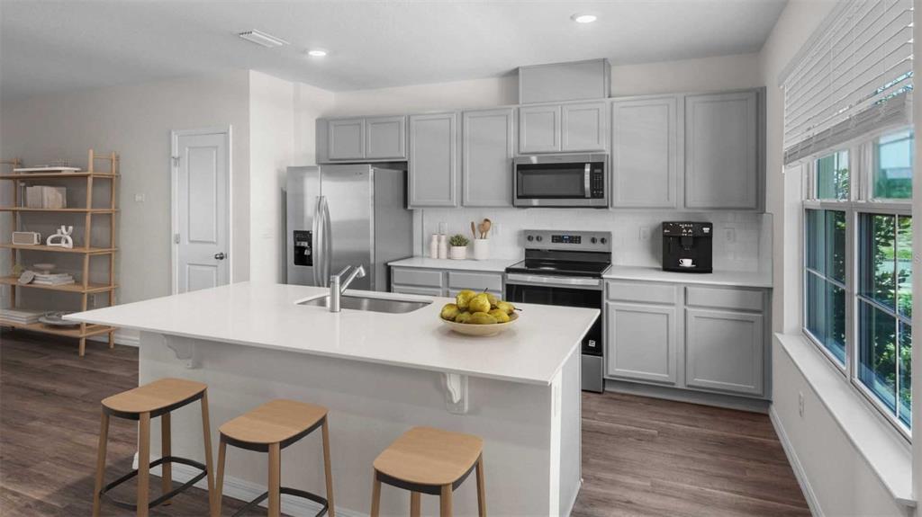 A kitchen features gray cabinets, white countertops, a center island with stools, and stainless appliances — 16570 BARBOURS CREEK WAY, WINTER GARDEN, FL