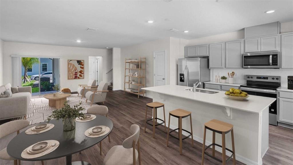 An open-concept kitchen and living area features light gray cabinetry, a white island, and wood-look flooring — 16570 BARBOURS CREEK WAY, WINTER GARDEN, FL