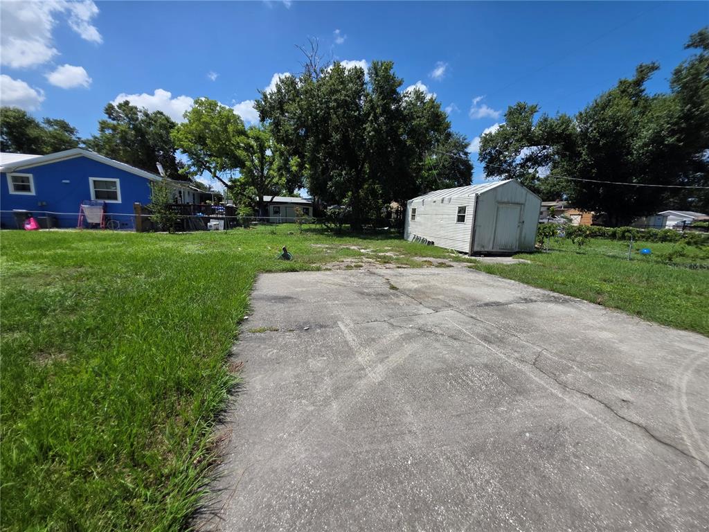 A concrete driveway leads to a backyard with a storage shed and a blue house — 2312 7TH ST E, BRADENTON, FL