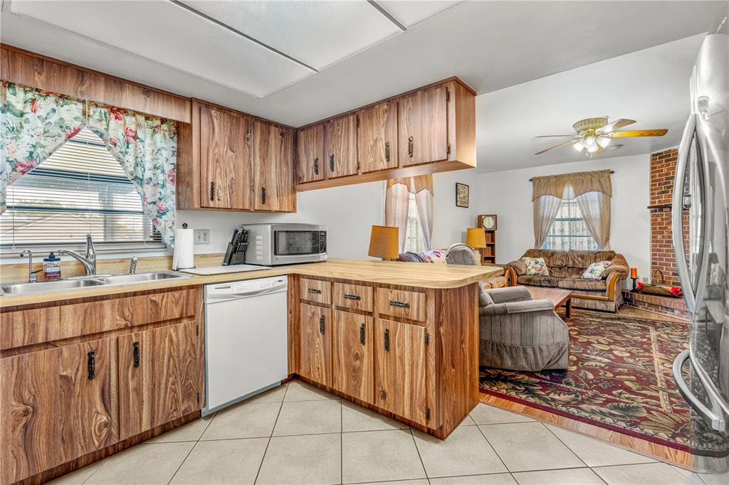 A kitchen with wood cabinets and a dishwasher opens into a living room with carpet — 2970 LAGOON AVENUE, DELTONA, FL