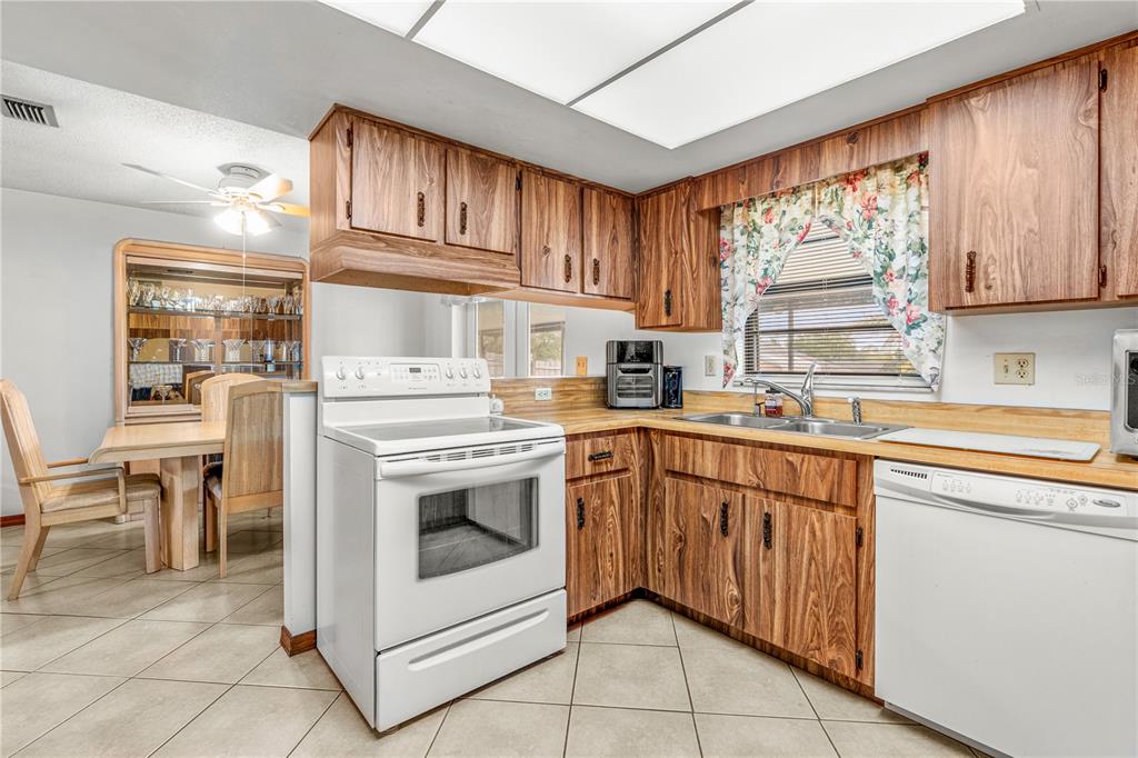 A kitchen with wood cabinets, white appliances, tile flooring, and an adjacent dining area — 2970 LAGOON AVENUE, DELTONA, FL