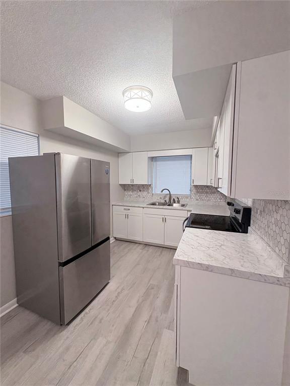 A kitchen features white cabinets, marble-look countertops, stainless steel appliances, and light wood-look flooring — 434 AVENUE D SE, WINTER HAVEN, FL