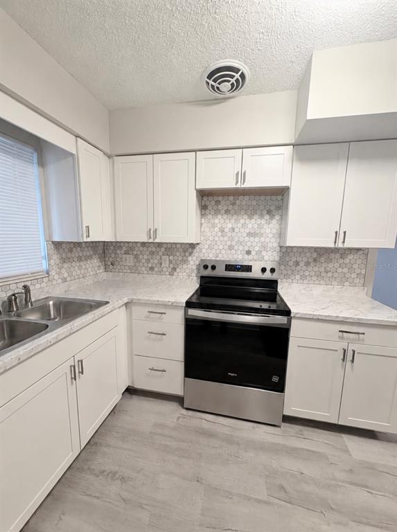 A kitchen features white cabinets, a marble-look countertop, a black stove, and hexagonal tile backsplash — 434 AVENUE D SE, WINTER HAVEN, FL