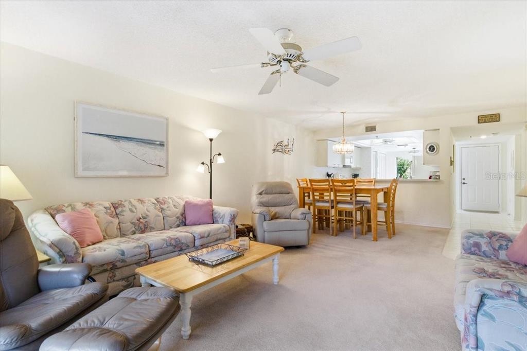 A living room with floral sofas, a wooden coffee table, and an adjacent dining area — 6713 STONE RIVER ROAD UNIT 103, BRADENTON, FL