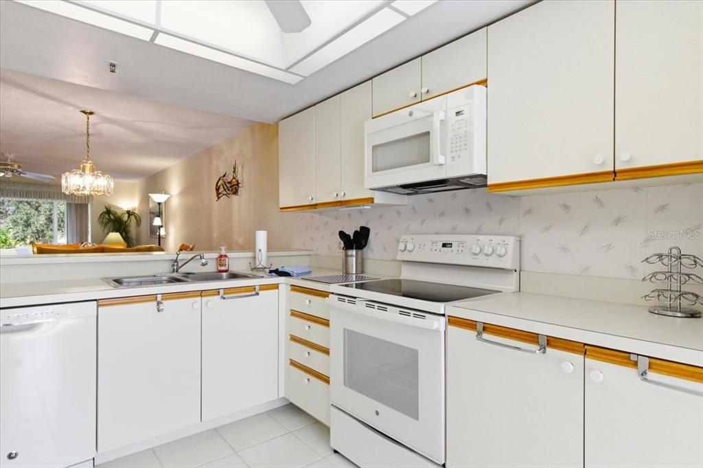A white kitchen features flat-panel cabinets with wood trim, white appliances, and a breakfast bar — 6713 STONE RIVER ROAD UNIT 103, BRADENTON, FL