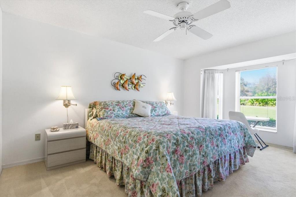 A bedroom features a floral bedspread, a ceiling fan, and a large window with views — 6713 STONE RIVER ROAD UNIT 103, BRADENTON, FL