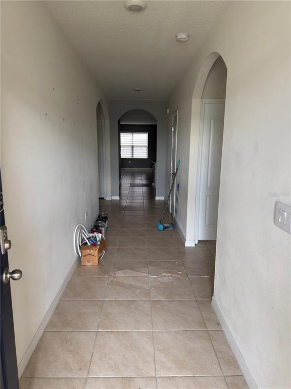 A tiled hallway leads from an entryway toward a distant windowed room with arched doorways — 1973 CARNOSTIE ROAD, WINTER HAVEN, FL