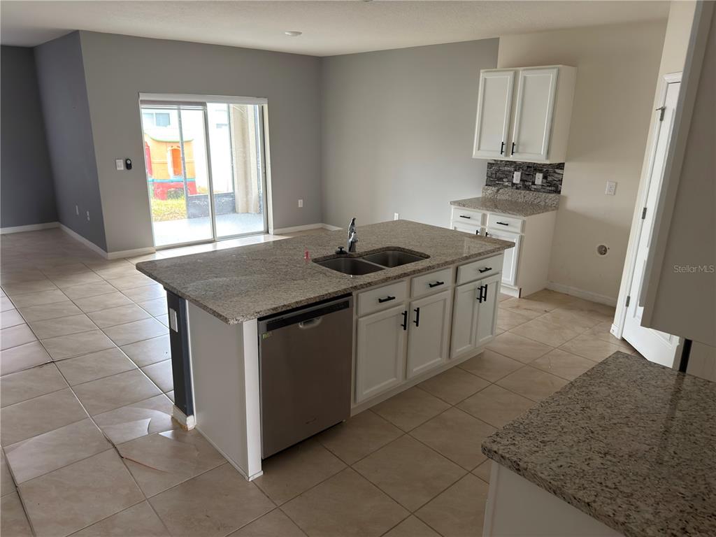 A kitchen features a granite-topped island with a stainless steel dishwasher and a sliding door — 1973 CARNOSTIE ROAD, WINTER HAVEN, FL