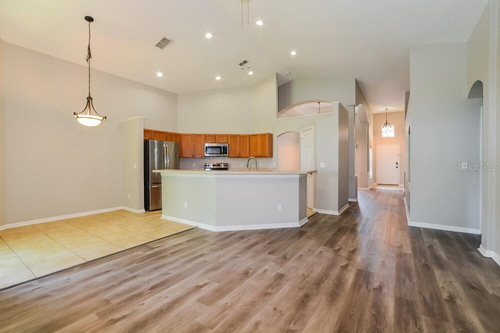 An open-concept kitchen and dining area features wood-look flooring, light gray walls, and cabinetry — 23 PATMORE ASH WAY, APOPKA, FL