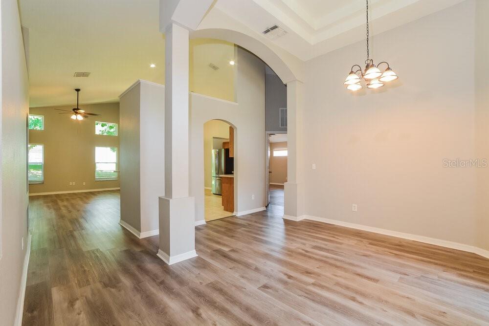 An open-concept dining area with light wood-look flooring, a chandelier, and a high ceiling — 23 PATMORE ASH WAY, APOPKA, FL