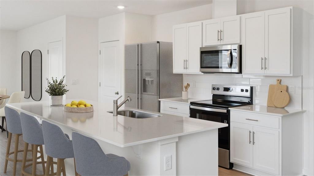 A modern kitchen features white cabinetry, stainless steel appliances, and a large quartz-topped island — 5168 BLANKET FLOWER STREET, APOPKA, FL
