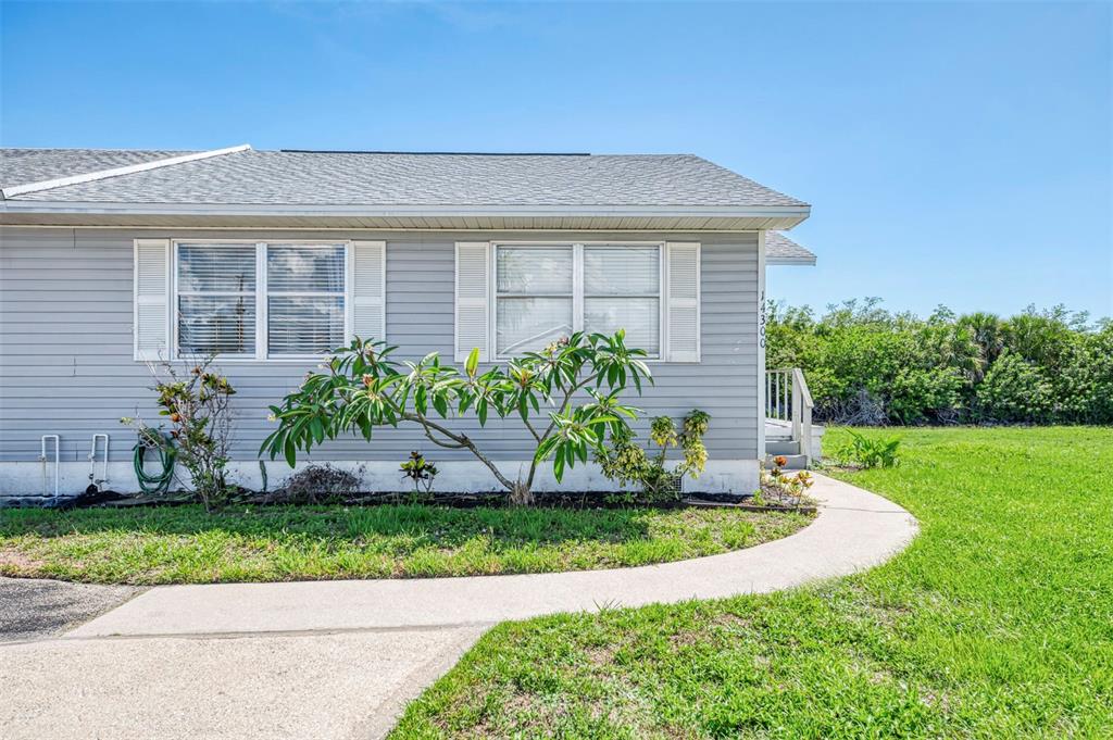 A gray-sided house exterior features a concrete walkway, a small tree, and green lawn — 14300 WORTHWHILE ROAD, PORT CHARLOTTE, FL