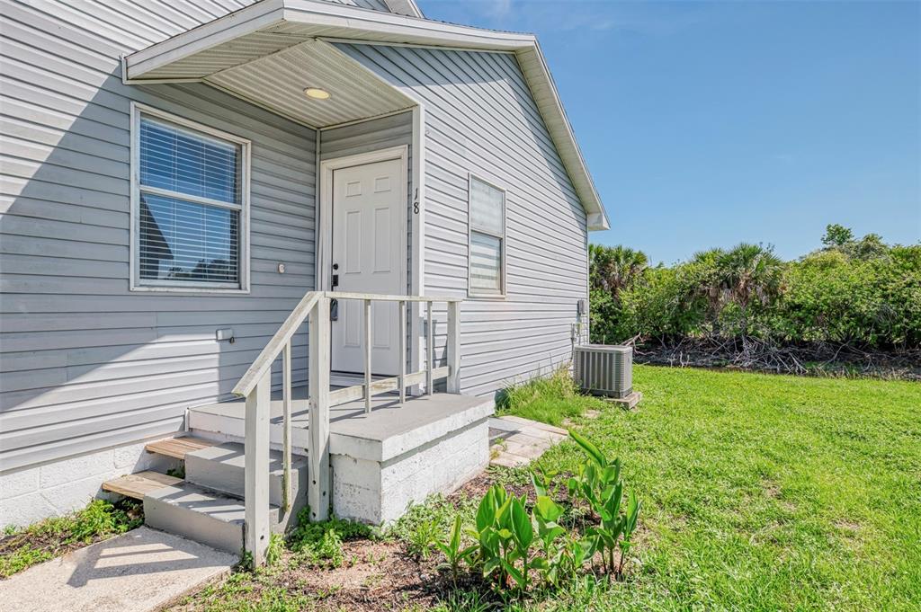 A gray-sided house exterior features a white front door, concrete steps, and a small porch — 14300 WORTHWHILE ROAD, PORT CHARLOTTE, FL