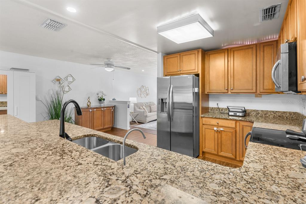 A kitchen with granite countertops, wooden cabinets, and stainless steel appliances overlooks a living area — 8243 PAMLICO STREET, ORLANDO, FL
