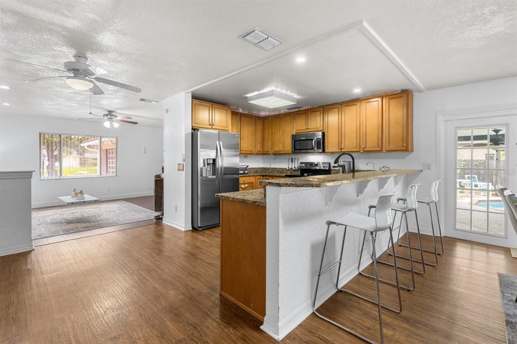 A kitchen with wood cabinets and granite countertops overlooks a living area with wood flooring — 8243 PAMLICO STREET, ORLANDO, FL