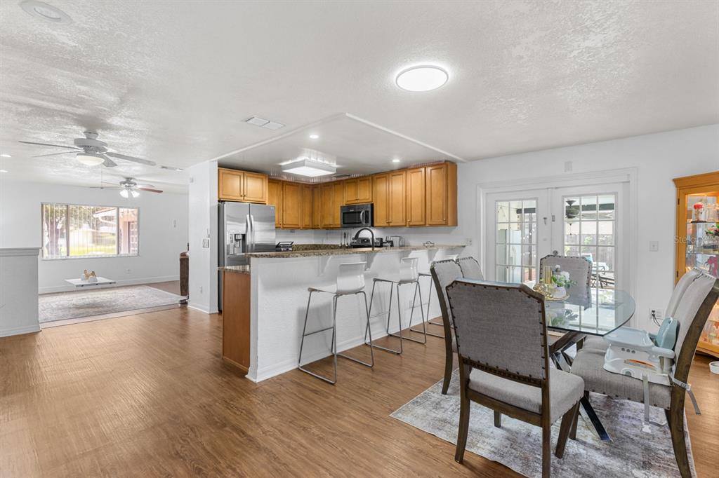A kitchen with wood cabinets and a granite breakfast bar overlooks a dining area — 8243 PAMLICO STREET, ORLANDO, FL