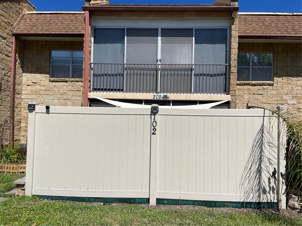 A tan vinyl privacy fence stands in front of a two-story building with a screened balcony — 2837 NE 3RD STREET UNIT 102, OCALA, FL