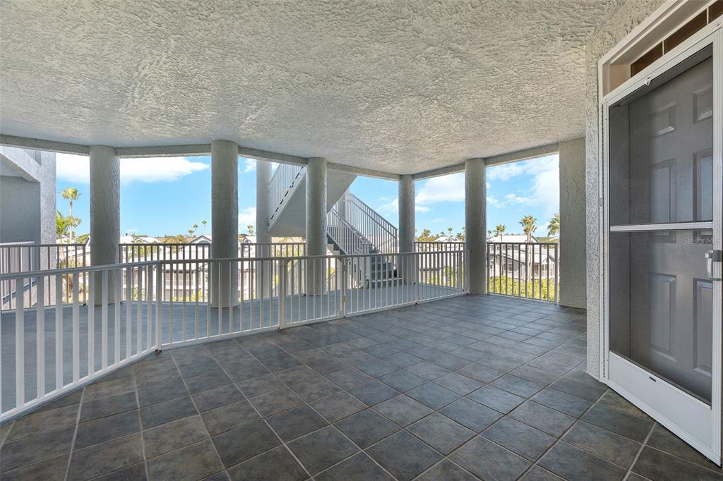 A covered balcony with tiled flooring, white railings, and concrete support columns overlooking a neighborhood — 1240 DOLPHIN BAY WAY UNIT 401, SARASOTA, FL
