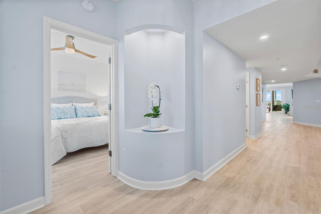A hallway with light wood flooring leads to a bedroom and an open living area — 1240 DOLPHIN BAY WAY UNIT 401, SARASOTA, FL