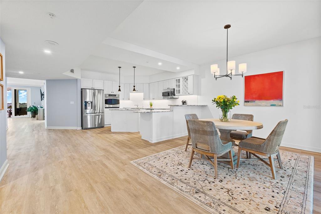 A bright, open-concept kitchen and dining area features white cabinetry, stainless appliances, and wood flooring — 1240 DOLPHIN BAY WAY UNIT 401, SARASOTA, FL