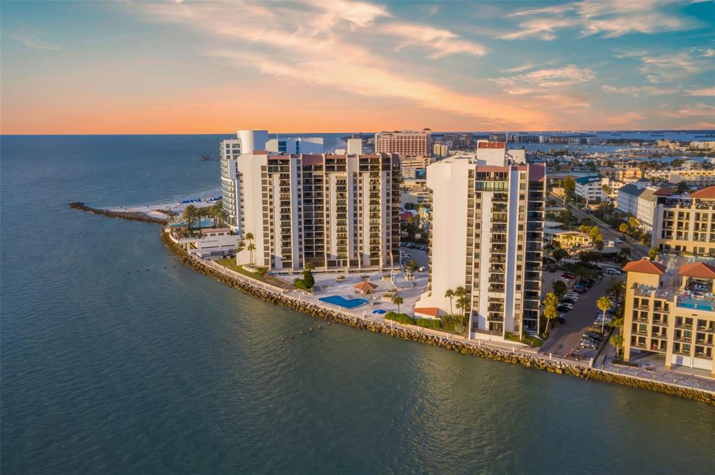 An aerial view of high-rise waterfront condominiums with swimming pools along a rocky shoreline — 440 S GULFVIEW BOULEVARD UNIT 1701, CLEARWATER BEACH, FL