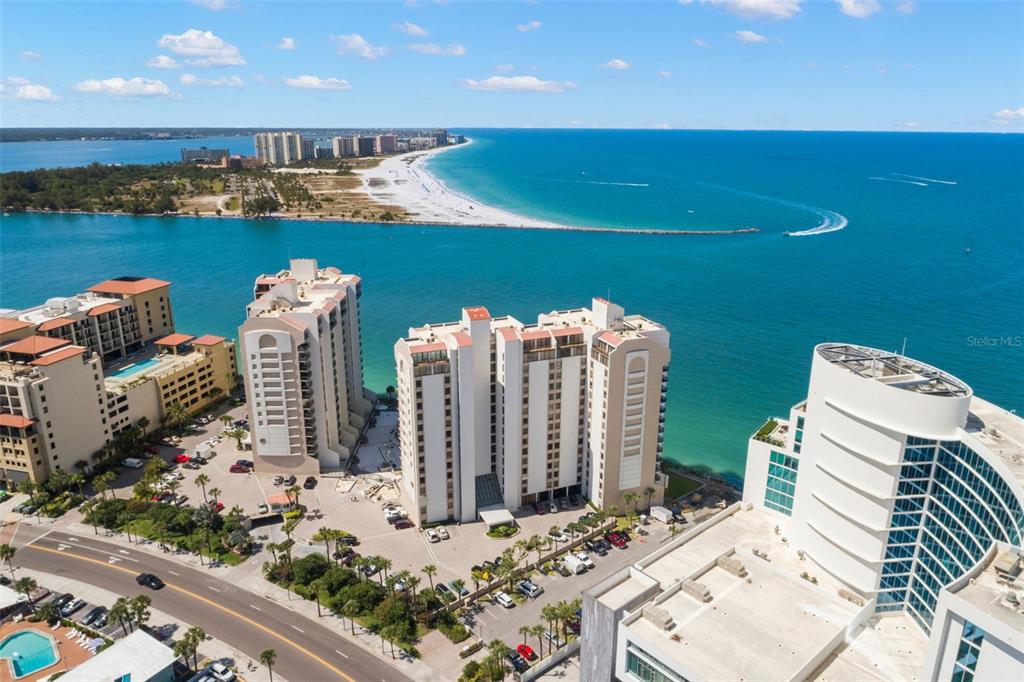 An aerial view shows high-rise condominiums situated along a coastal waterway near a sandy beach — 440 S GULFVIEW BOULEVARD UNIT 1701, CLEARWATER BEACH, FL