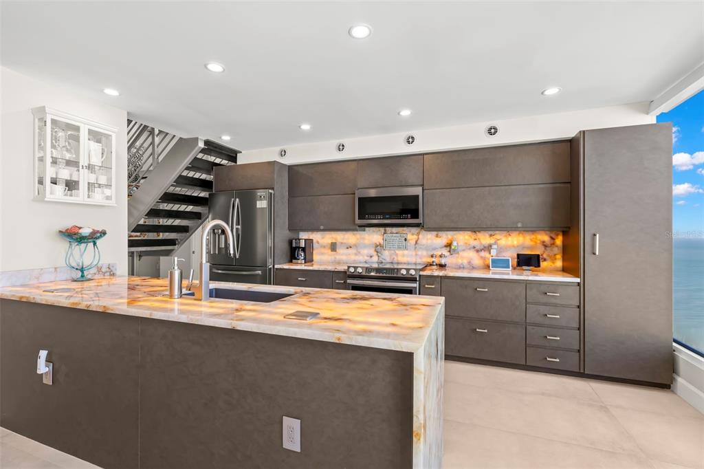 A modern kitchen features a backlit stone island, dark cabinetry, and a staircase to the left — 440 S GULFVIEW BOULEVARD UNIT 1701, CLEARWATER BEACH, FL