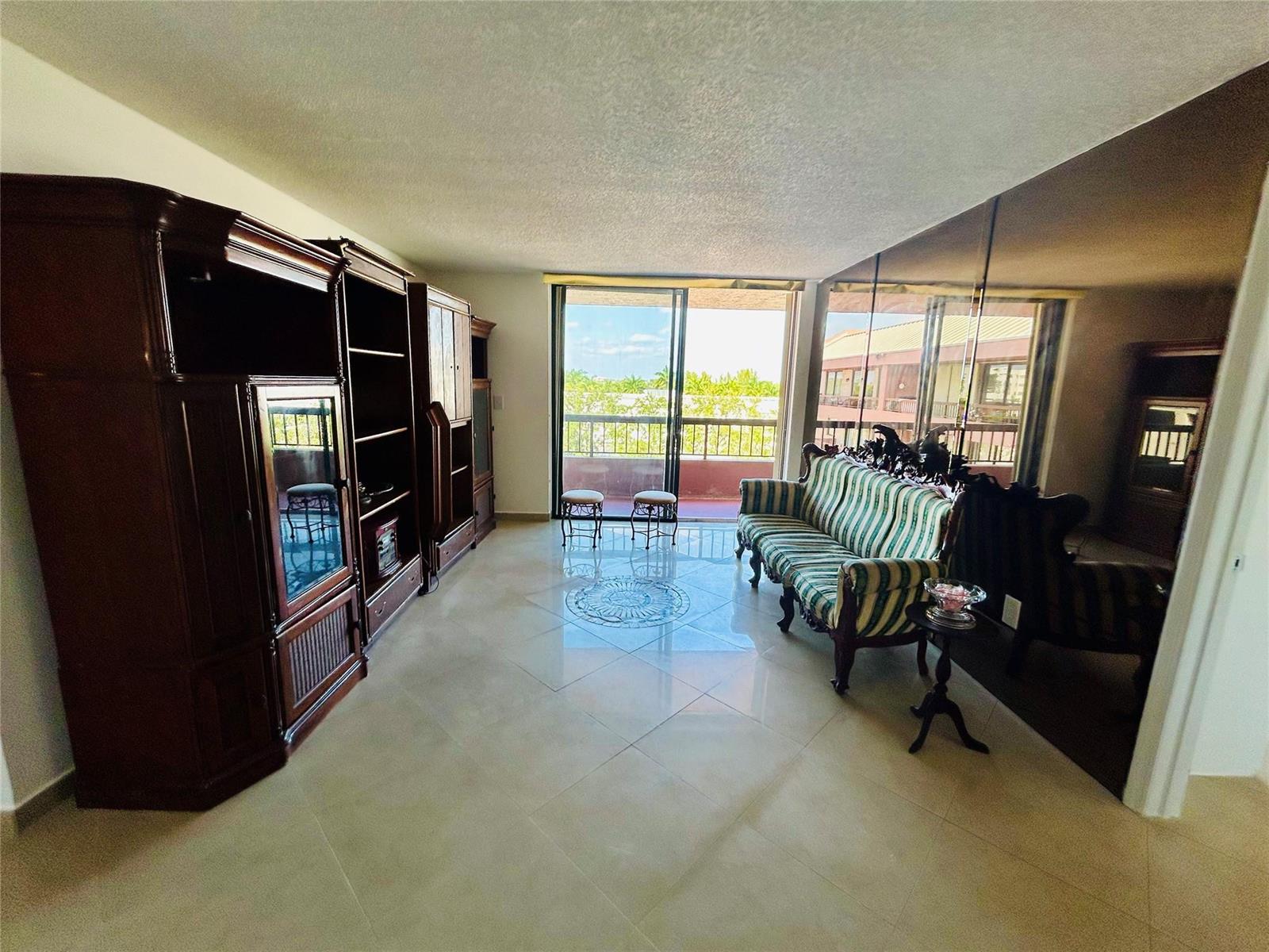 A living room features tile flooring, a large wooden entertainment center, and a mirrored wall — 7040 Coral Way # 501, Miami FL 33155, MIAMI, FL