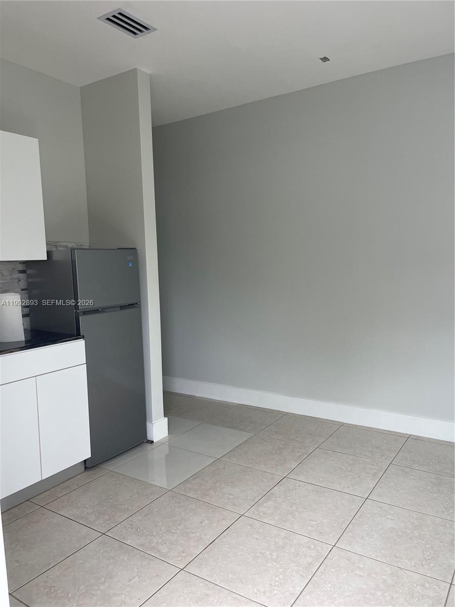 A kitchen area features a gray refrigerator, white cabinets, and light-colored tile flooring — 14554 SW 161 Ct, Miami FL 33196, MIAMI, FL