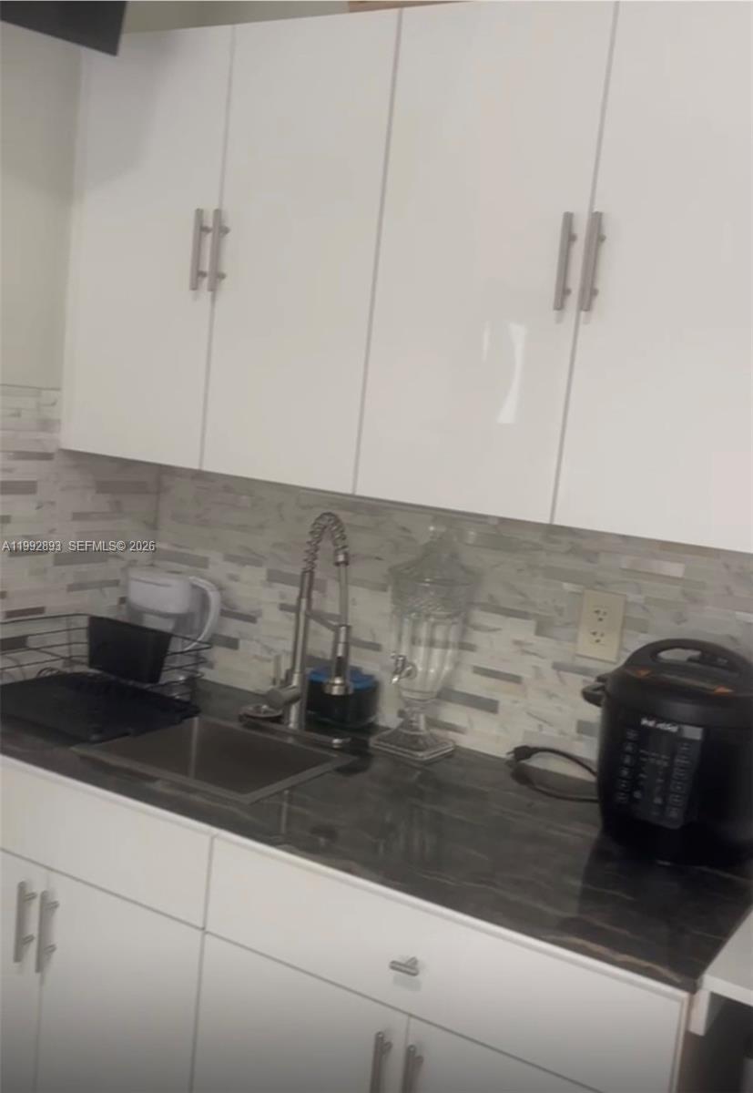 A kitchen features white cabinets, a dark countertop, and a light-colored tiled backsplash — 14554 SW 161 Ct, Miami FL 33196, MIAMI, FL