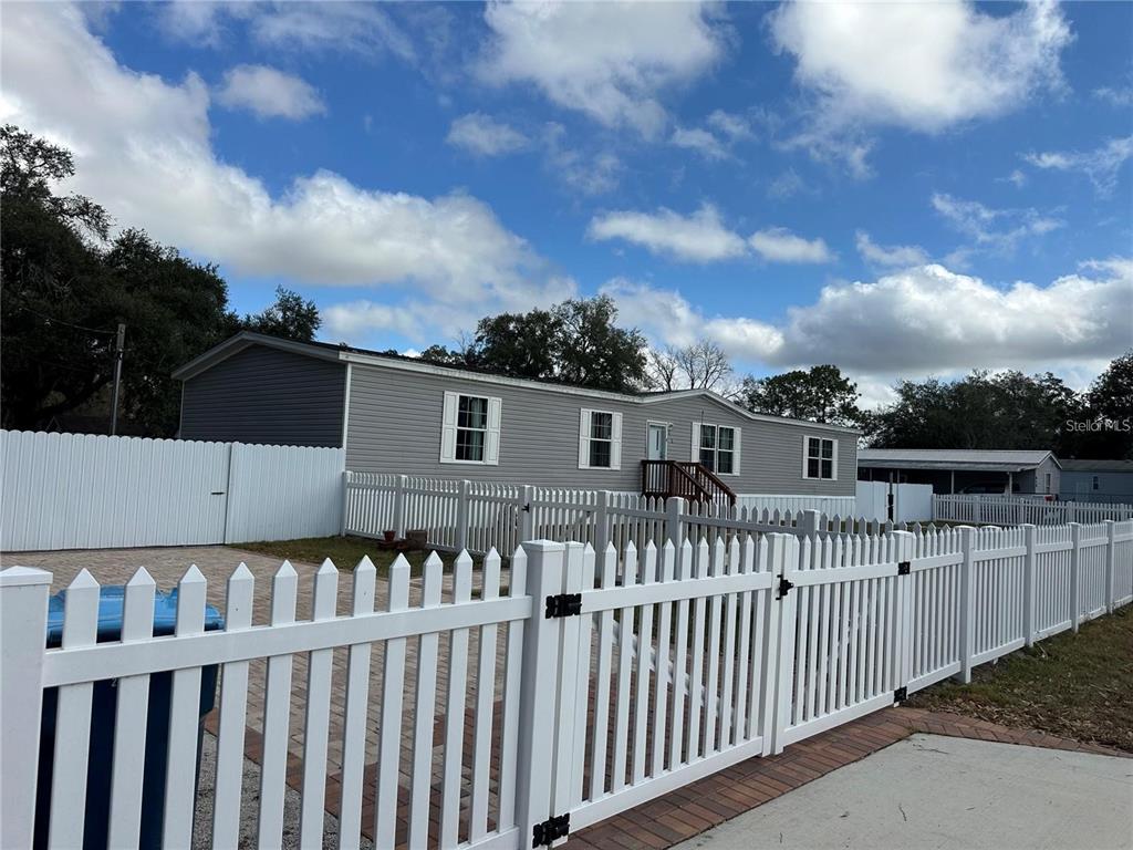 A gray manufactured home sits behind a white picket fence with a paved driveway — 618 1 ST STREET, POLK CITY, FL