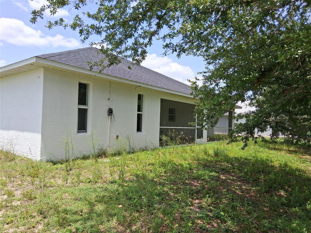 A side view of a white stucco house with a screened-in porch and overgrown lawn — 850 SW 15TH STREET, CAPE CORAL, FL