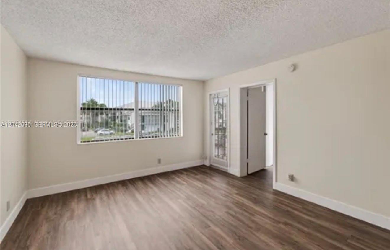 An empty room features wood-look flooring, beige walls, a large window, and a glass door — 738 Executive Center Dr # 23, West Palm Beach FL 33401, WEST PALM BEACH, FL