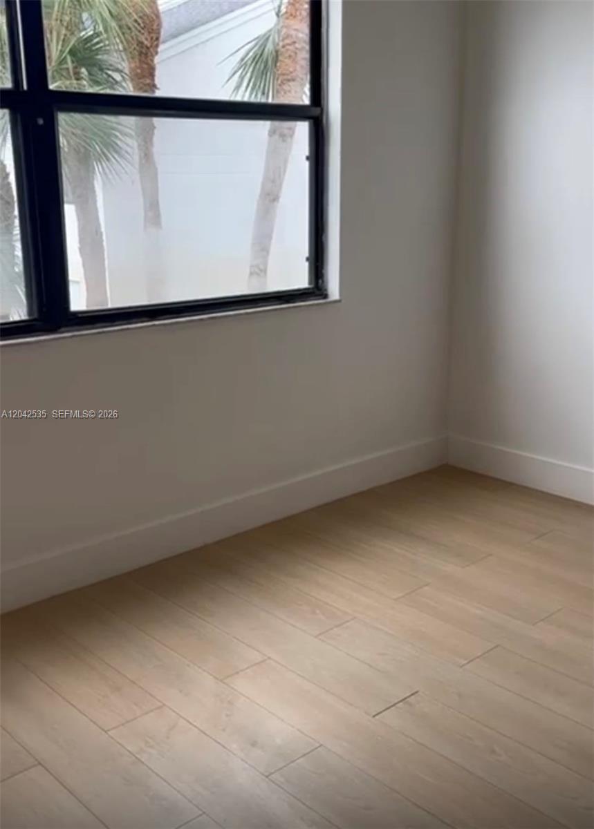 An empty room features light wood-look flooring, white walls, and a window overlooking palm trees — 738 Executive Center Dr # 23, West Palm Beach FL 33401, WEST PALM BEACH, FL