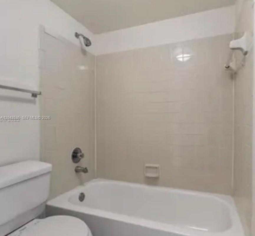 A bathroom features a white bathtub with a shower head and light-colored tiled walls — 738 Executive Center Dr # 23, West Palm Beach FL 33401, WEST PALM BEACH, FL