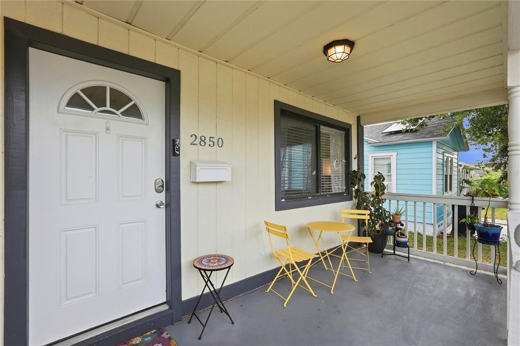 A covered front porch features a white door, yellow bistro set, and gray painted floor — 2850 15TH AVENUE N, ST PETERSBURG, FL
