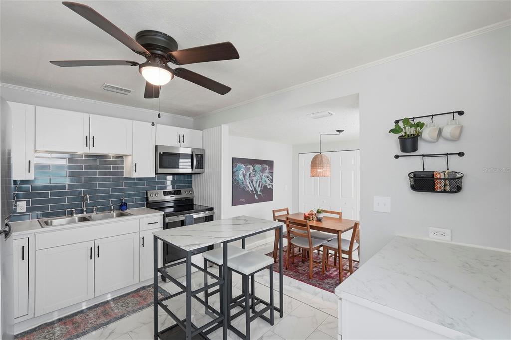 A kitchen with white cabinets, a marble-topped island, blue tile backsplash, and an adjacent dining area — 2850 15TH AVENUE N, ST PETERSBURG, FL