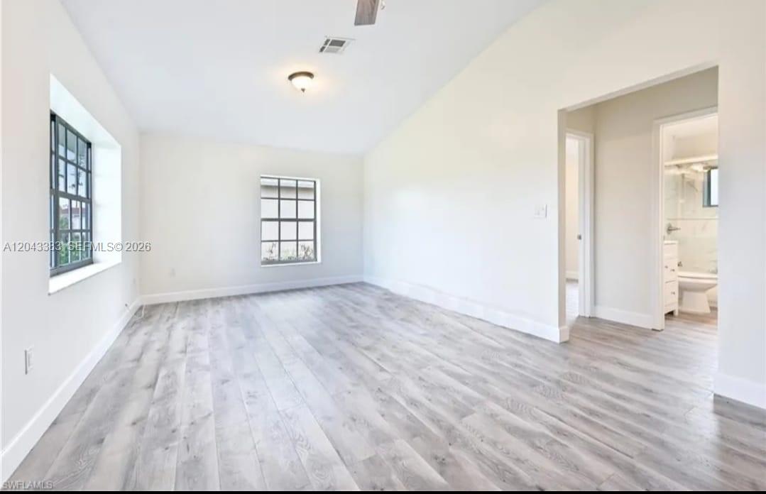 An empty room with white walls, light wood-look flooring, two windows, and an attached bathroom — 2830 NE 4th Ave, Naples FL 34120, NAPLES, FL