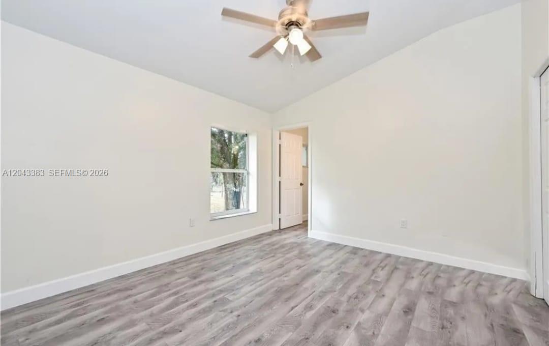 A bedroom features light-colored walls, a ceiling fan, and gray wood-look flooring — 2830 NE 4th Ave, Naples FL 34120, NAPLES, FL